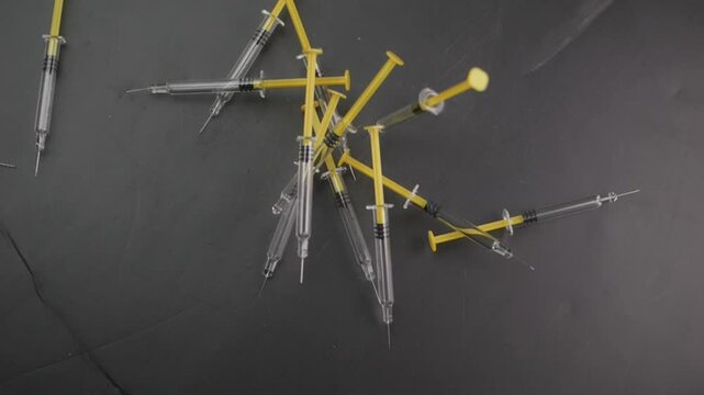 Slow-motion shot of disposable syringes dropping onto a dark matte surface, designed for vaccinations or self-administered subcutaneous injections.
