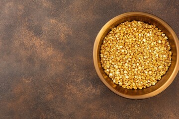 A wooden bowl filled with shiny, golden grains sits on a textured brown surface, creating a warm and inviting visual.
