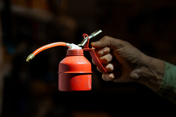 Hand Holding Red Metal Oil Canister with Lever Pump Dispenser on Dark Background