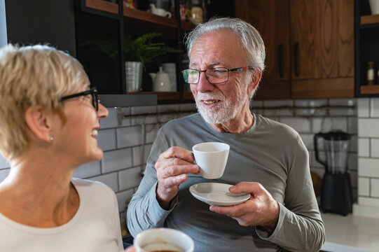 A happy senior couple enjoys a morning coffee together in their cozy kitchen, sharing a warm conversation and cherishing the present moments with love and affection.