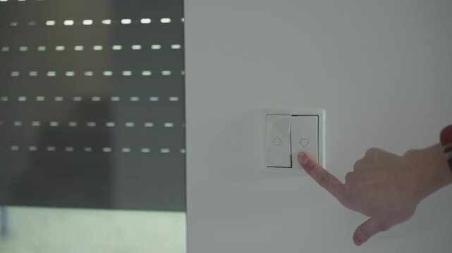 Woman pressing a wall switch to control electric window blinds in a modern home. Smart home automation, energy efficiency, and convenience in daily life