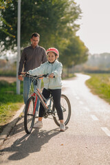 Fototapeta premium Father watching daughter learning to ride bicycle in park