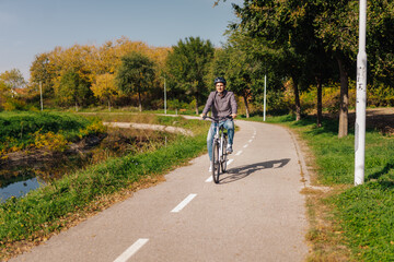 Obraz premium Young man riding bicycle in a park near a river during a sunny autumn day