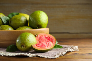 Fresh cut and whole guava fruits on wooden table, closeup. Space for text