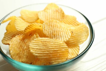 Tasty potato chips in bowl on white table, closeup