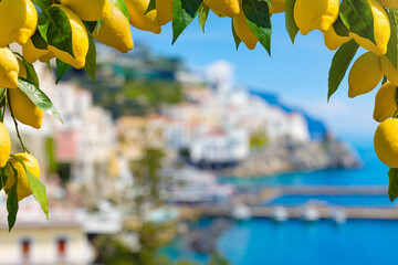 Fresh lemons framing image with blurred view of Amalfi, Italy, in background. Background features blurred coastal view of Amalfi, Italy, with blue sea and colorful buildings