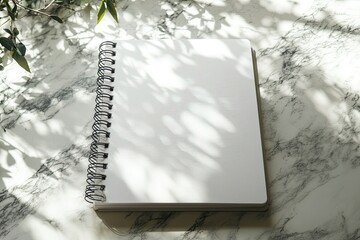 Blank Spiral Notebook on Marble Surface with Leaf Shadows