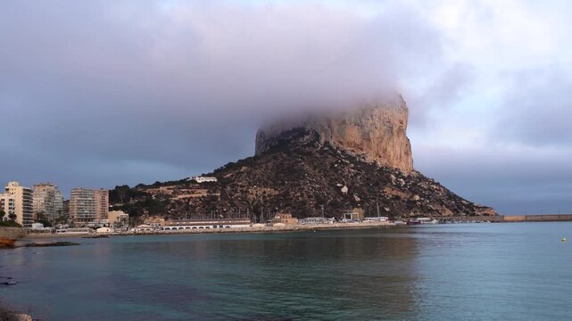 View of Pe&ntilde;&oacute;n de Ifach mountain. Beautiful pink colours reflecting on the mountain peak at sunset. Peak of the mountain in fog. Natural Park in Calpe city, Alicante Province, Spain. Travel destination
