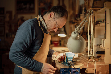 Luthier carefully working on violin scroll in his workshop