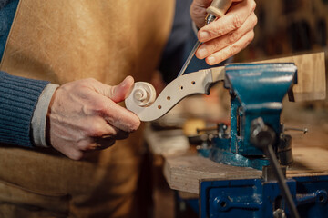 Luthier carefully crafting violin scroll using precise tools in workshop