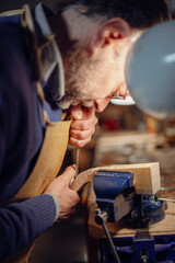 Luthier carefully working on violin scroll in workshop using small chisel and vise