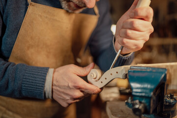 Luthier working on violin scroll using gouge and vise in workshop