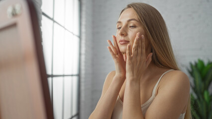 Woman gently touching face in bright living room, reflecting beauty routine and serene self-care moment indoors as natural light fills the space with peaceful ambiance.
