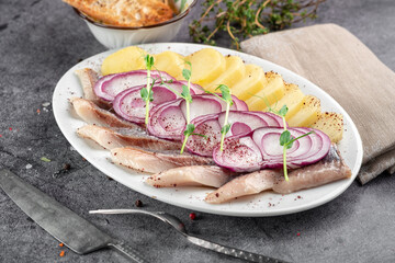 Atlantic herring marinated in salt, sliced, served on a white plate with onions, potatoes and herbs, close up