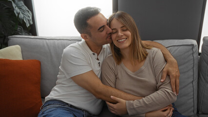 Hispanic couple sharing a loving moment with man kissing woman on cheek, sitting comfortably in a cozy living room setting, highlighting warmth and intimate connection at home.