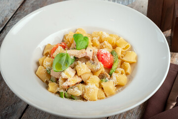 Rigatoni pasta with chicken, mushrooms and fresh tomatoes, served on a white plate with parmesan and basil