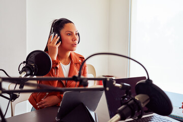 Radio host recording a podcast in a professional studio, speaking into a microphone and wearing...