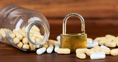 Pills with jar and padlock on the table. Drug addiction, medicine banner or background.