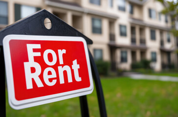 A red and white for rent sign is prominently displayed in front of a well-maintained residential building, indicating availability
