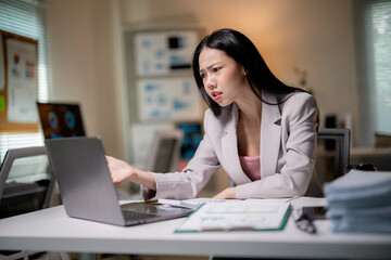 Young Asian businesswoman showing frustration while working late at night in the office with her laptop