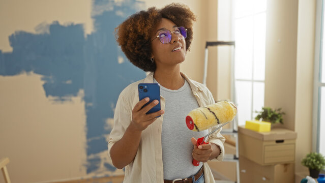 Woman painting new apartment living room holding phone roller smiling enjoying fresh start home renovation project creative process indoors