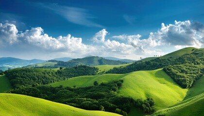A picturesque countryside scene featuring undulating green hills, dense woodlands, and a brilliant blue sky dotted with soft, drifting clouds.