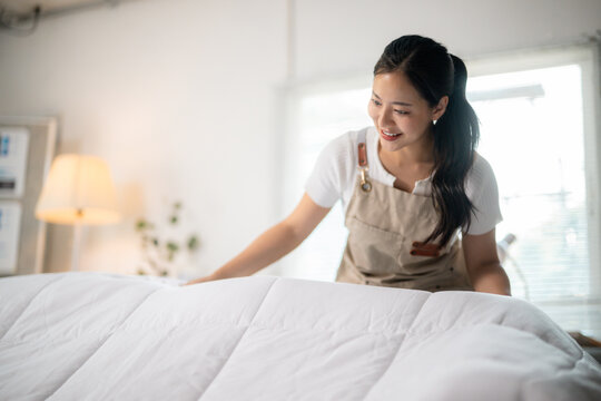 Smiling maid making bed, arranging blanket in hotel room