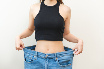 Shape slender, thin waist, slim fit asian young woman, showing body shape her weight loss, happy wearing in big, large or oversize jeans, excess lose by diet and exercise. Healthy lifestyle concept