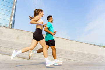 Couple jogging together in urban setting under clear blue sky during sunny day