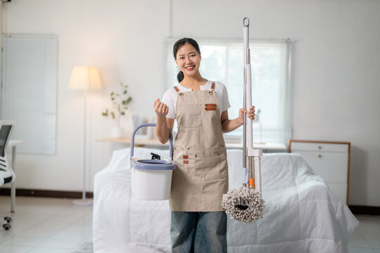 Happy housekeeper with cleaning products smiling at camera in bedroom
