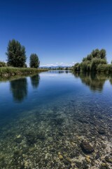 Obraz premium Calm river waters reflect clear blue skies and lush vegetation