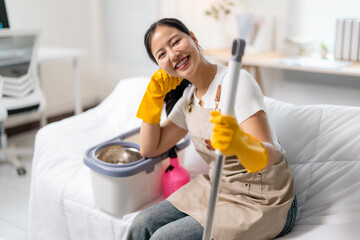 Cheerful asian cleaning professional relaxing on couch, gripping mop and smiling