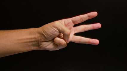 Man showing three fingers against a black background with a closeup focus on the hand in color.