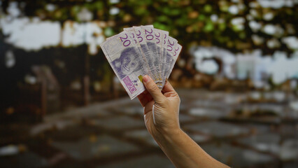 Hand holding swedish krona banknotes outdoors in an urban street setting, reflecting a business and investment theme in a city environment with a man involved.