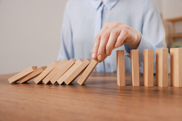 Woman stopping wooden blocks from falling at table, closeup. Domino effect