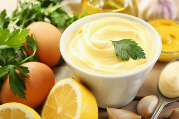 Delicious mayonnaise sauce in bowl and ingredients on table, closeup