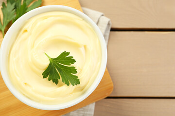 Delicious mayonnaise sauce with parsley in bowl on wooden table, top view. Space for text