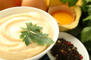 Delicious mayonnaise sauce with parsley in bowl and ingredients on table, closeup