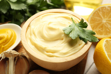 Delicious mayonnaise sauce with parsley in bowl, lemon and garlic on table, closeup