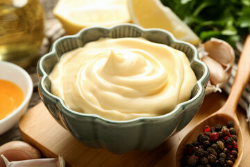 Delicious mayonnaise sauce in bowl and ingredients on table, closeup