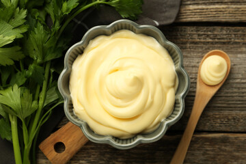 Delicious mayonnaise sauce in bowl and parsley on wooden table, top view