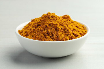 Turmeric powder in bowl on white table, closeup