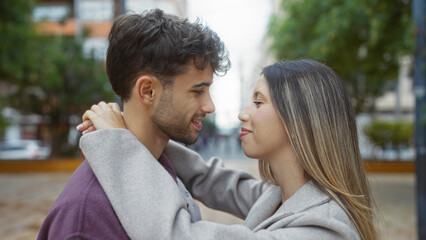 Couple embracing outdoors with man and woman gazing lovingly in an urban street setting, expressing relationship and romance against a city backdrop.