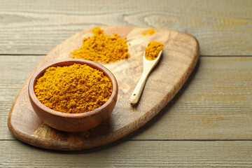 Turmeric powder in bowl and spoon on wooden table, closeup