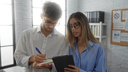 Man and woman collaborating in a modern office, reviewing documents and using digital tablet, showcasing teamwork and productivity in a professional setting.
