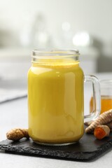 Delicious turmeric latte with honey and rhizomes on grey table, closeup