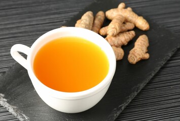 Aromatic turmeric tea and rhizomes on black table, closeup