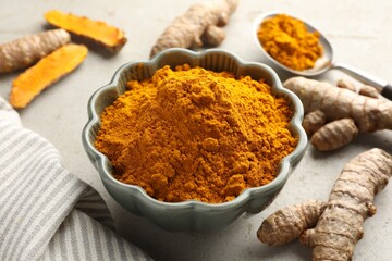 Aromatic turmeric powder in bowl and fresh roots on light grey table, closeup