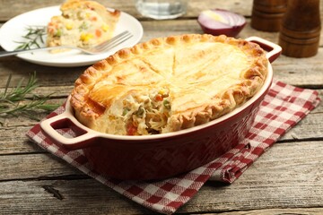 Tasty homemade pie with chicken and vegetables in baking dish on wooden table, closeup