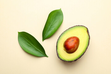 One cut ripe avocado and leaves on beige background, top view